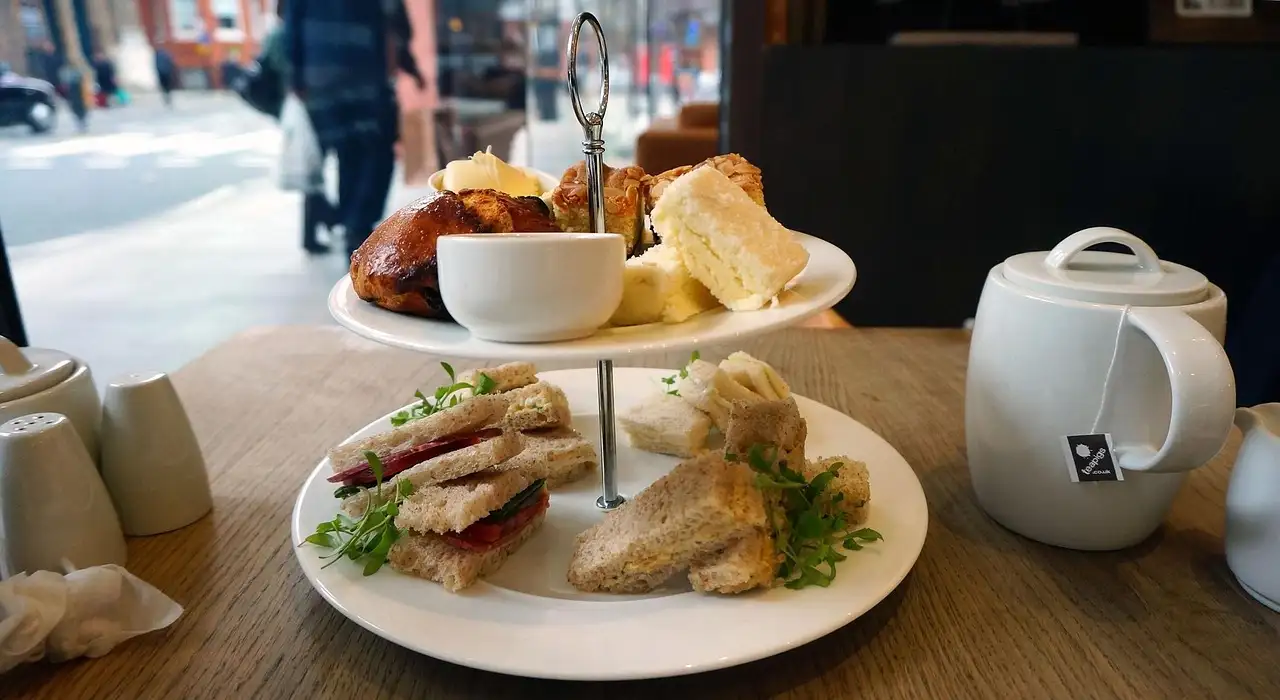 A tiered stand with sandwiches and scones next to a white teapot