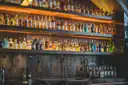 Shelves of bottles lit up behind a long bar