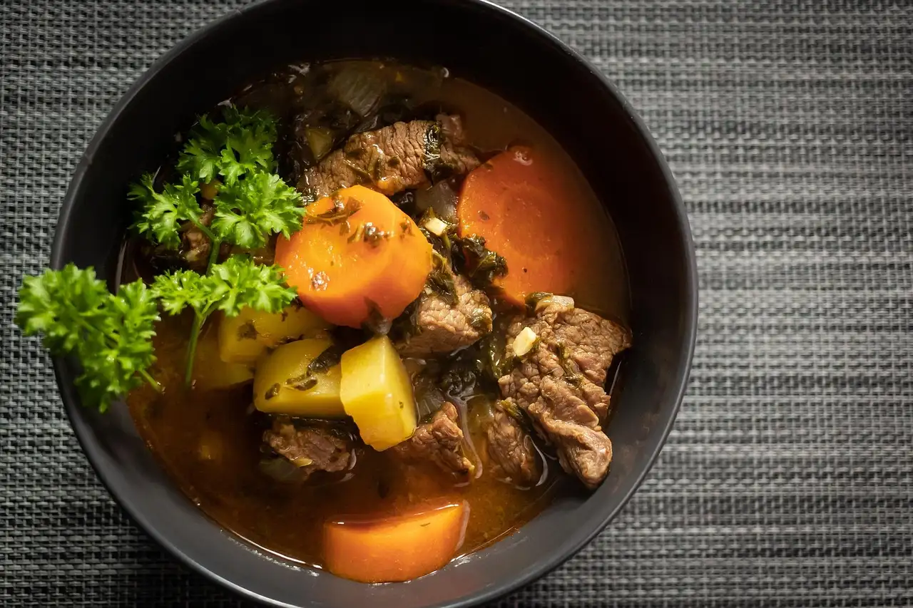 A bowl of beef stew with carrots, potatoes and parsley