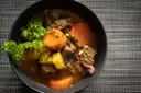 A bowl of beef stew with carrots, potatoes and parsley