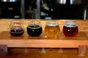 Four small glasses of beer, dark to amber, on a wooden board