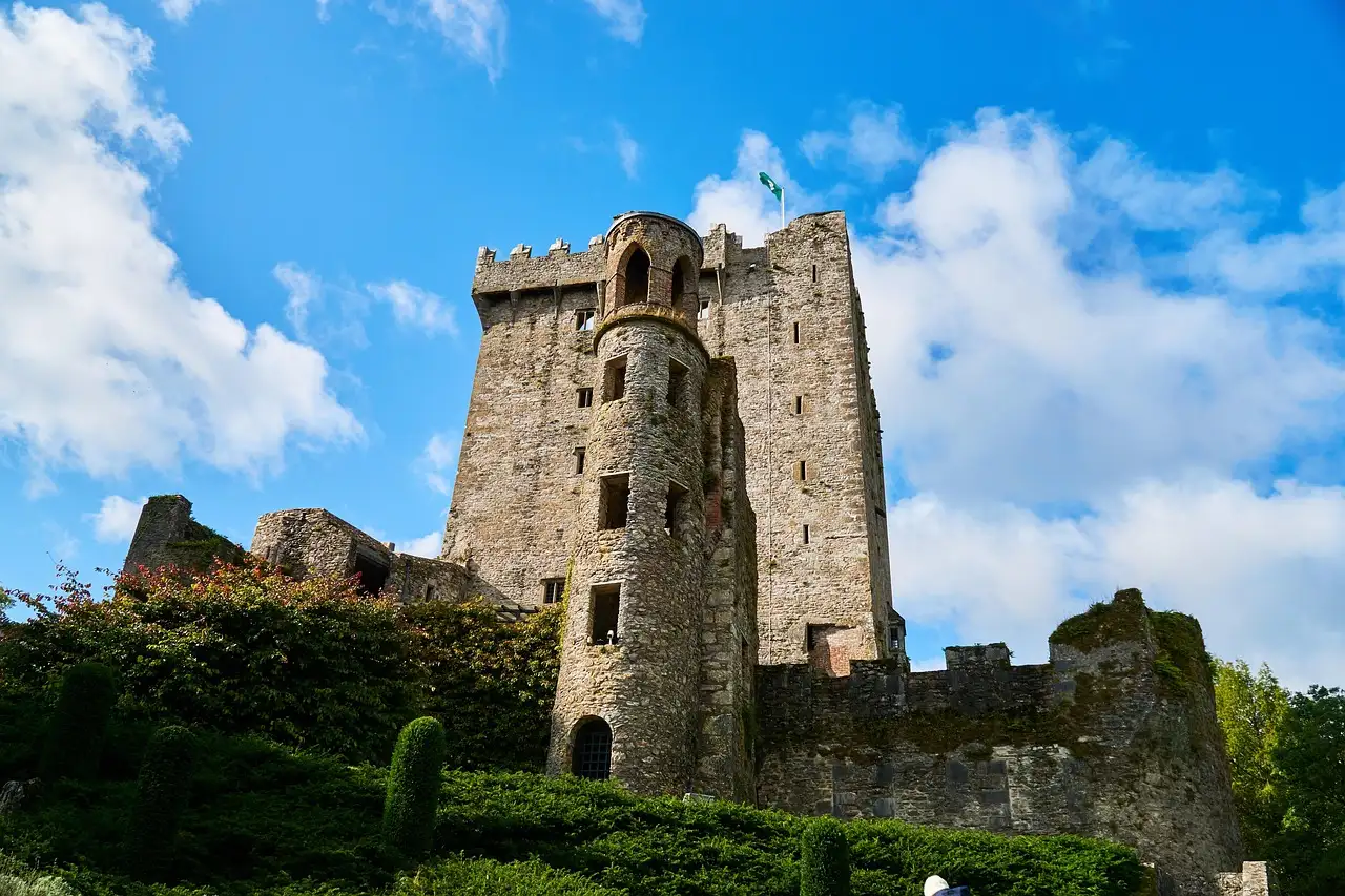 The stone keep of Blarney Castle above trees and green bushes under a blue sky