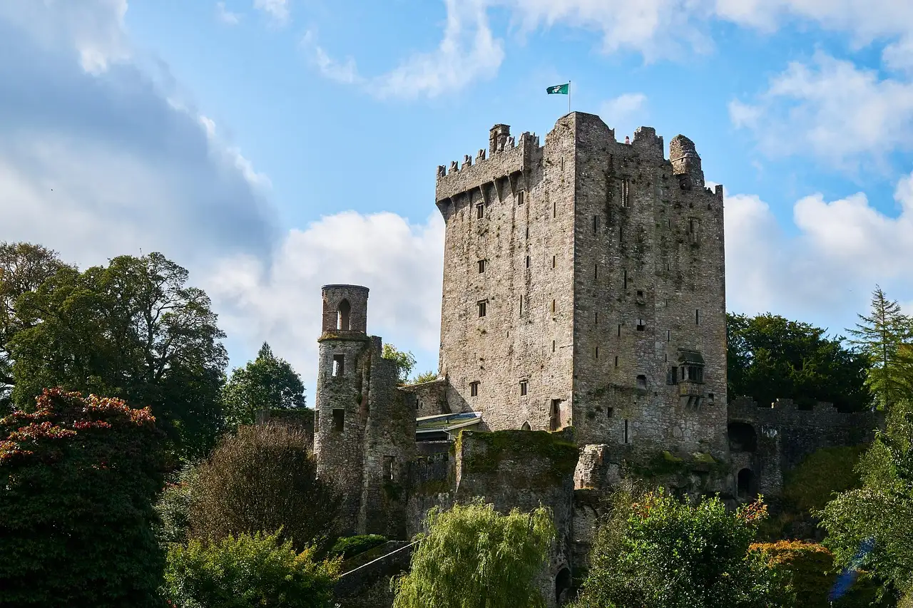 The stone keep of Blarney Castle above trees and gardens, under a blue sky