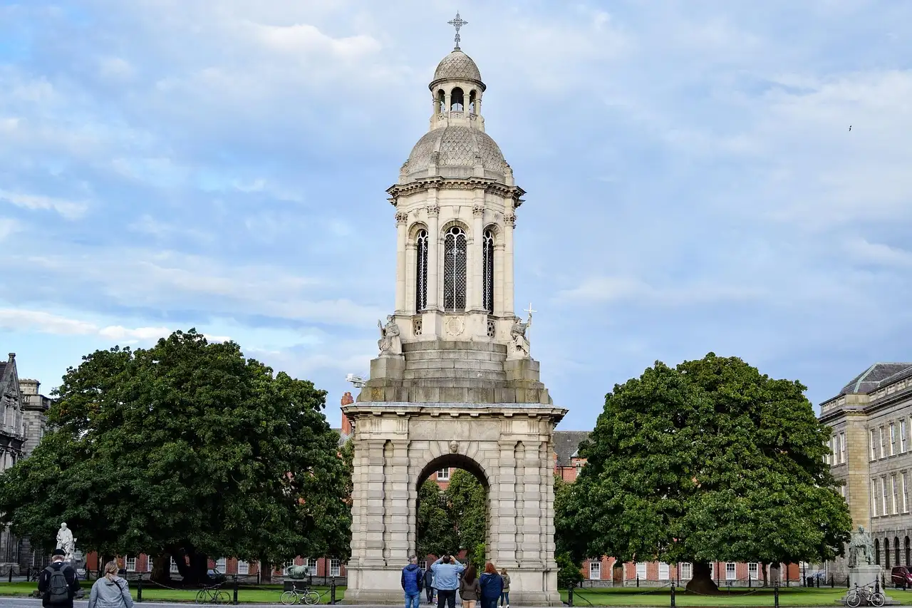 The stone bell tower in Trinity College's front square, on a green lawn under blue sky