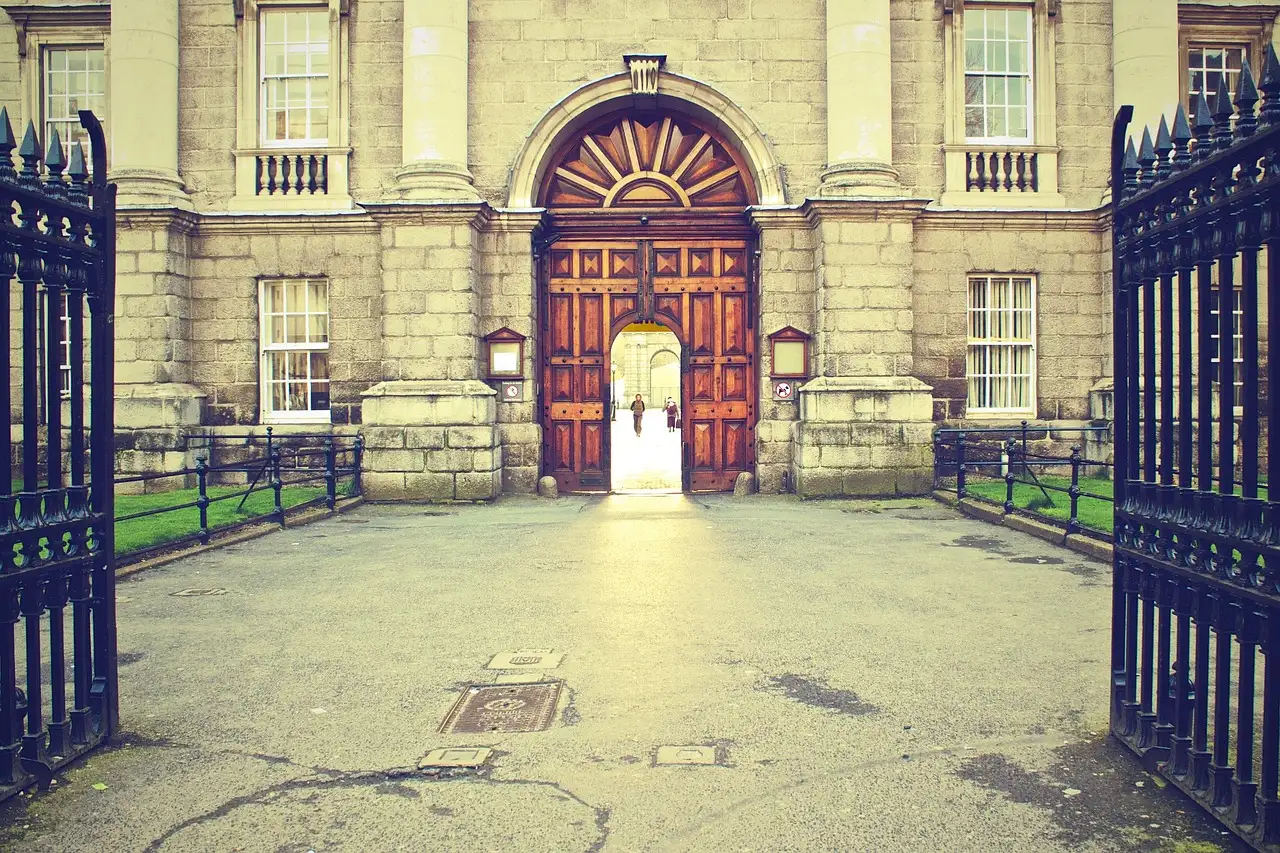 The arched wooden door and open iron gates of a Trinity College archway onto a paved courtyard