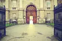 The arched wooden door and open iron gates of a Trinity College archway onto a paved courtyard
