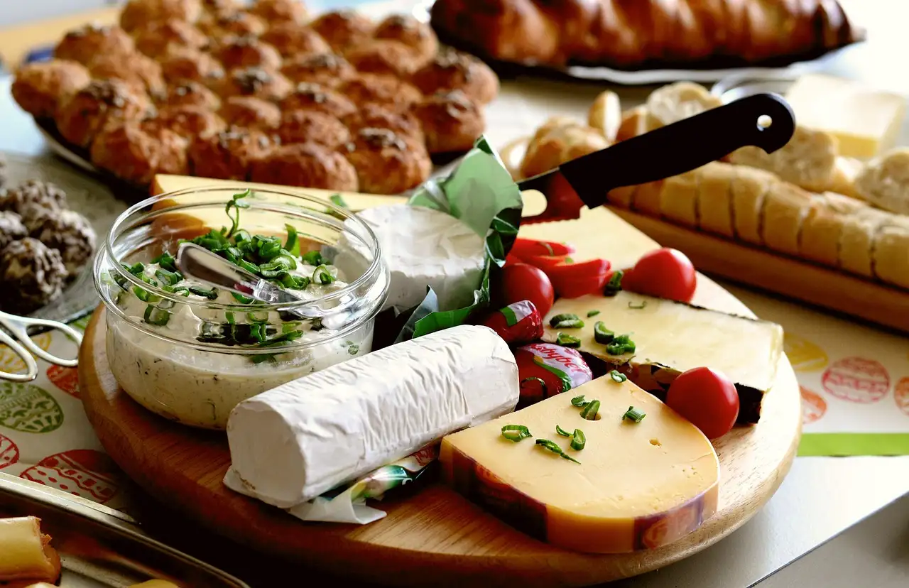 A wooden board with cheeses and a glass jar of dip