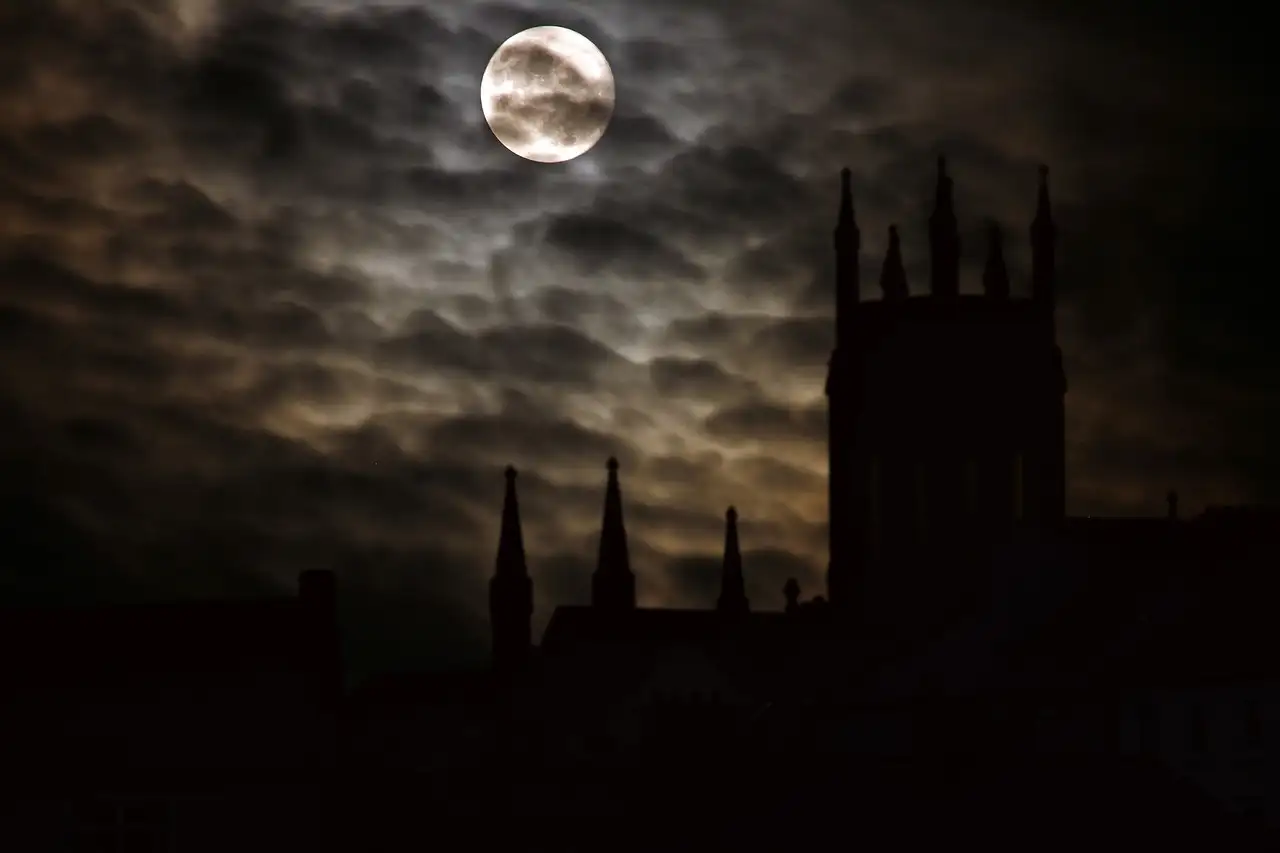Church towers in black outline under a full moon and dark clouds