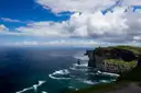 The dark Cliffs of Moher under white clouds, with low cloud along the sea