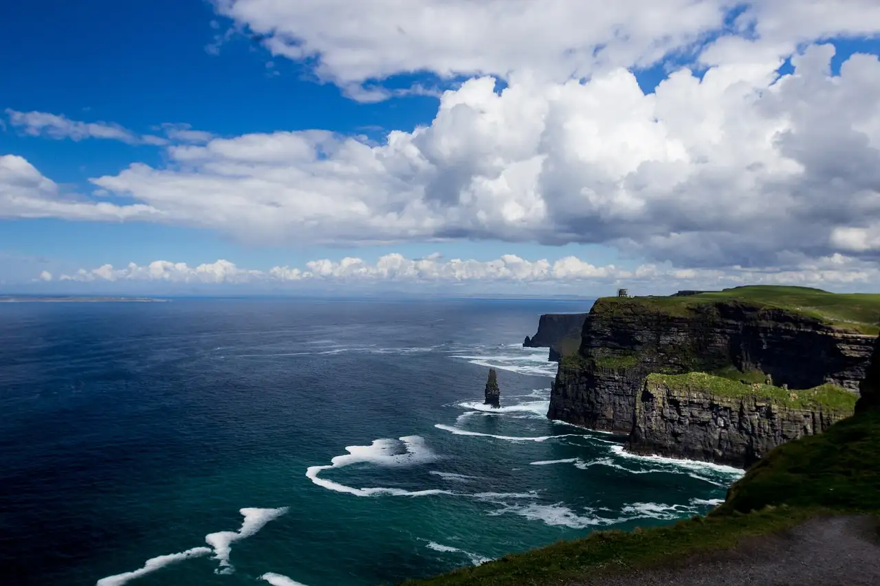 The dark Cliffs of Moher under white clouds, with low cloud along the sea