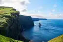 The Cliffs of Moher above a blue Atlantic, with a sea stack below and white clouds over the headlands