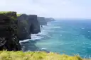 The Cliffs of Moher in a long line above turquoise water, seen from the grassy clifftop