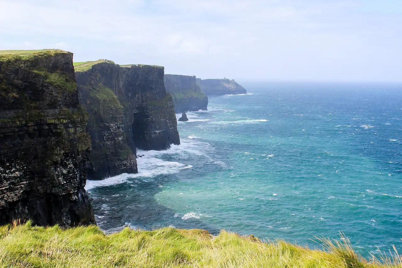 The Cliffs of Moher in a long line above turquoise water, seen from the grassy clifftop
