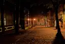 An empty cobbled street at night, lit by old street lamps
