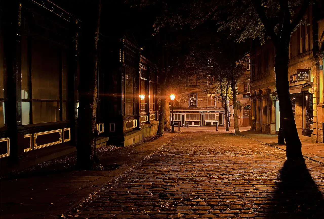 An empty cobbled street at night, lit by old street lamps