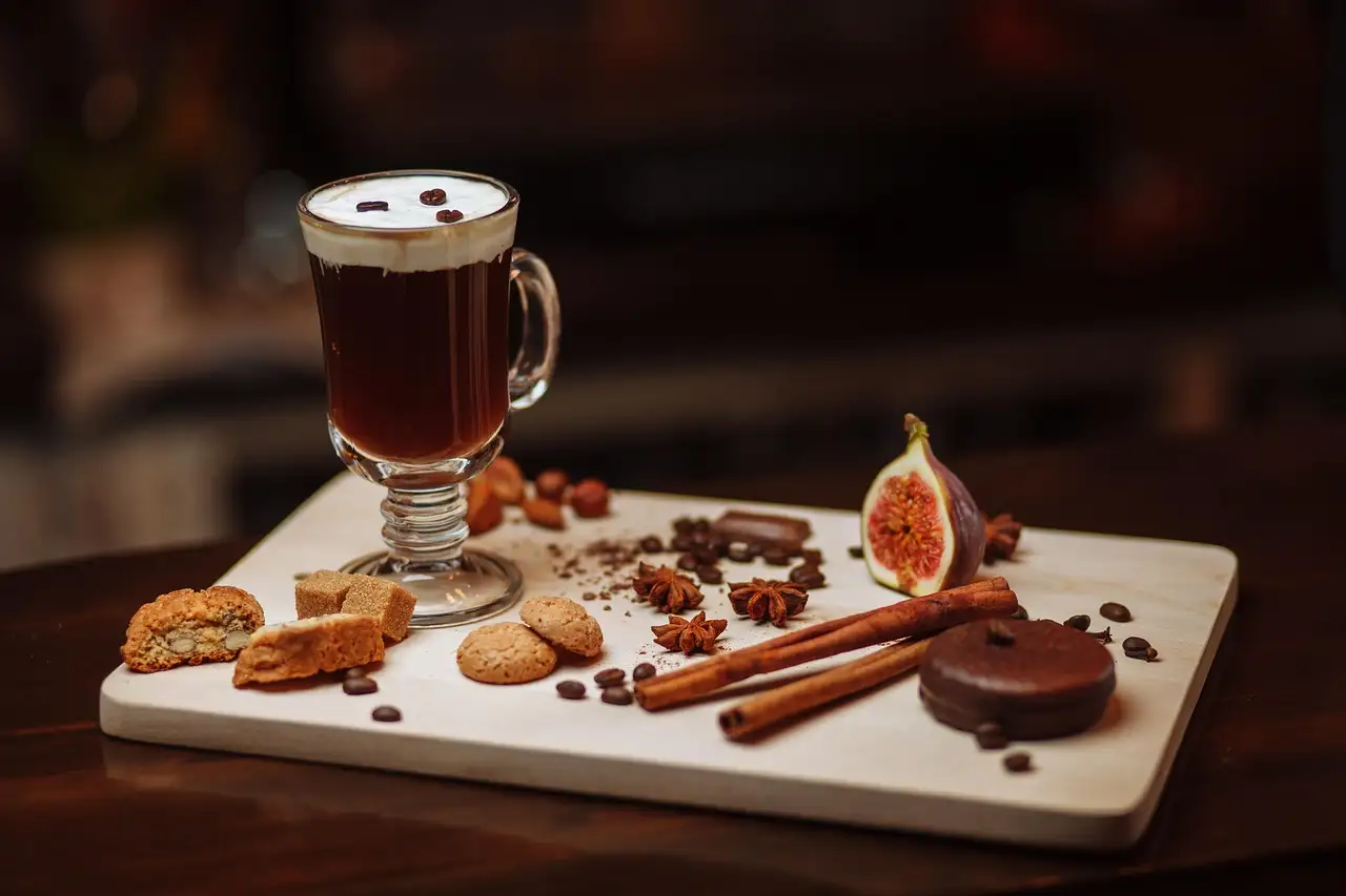 An Irish coffee in a glass mug on a board with biscuits and spices