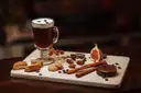 A glass of coffee with a creamy top on a board with biscuits and spices