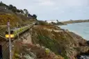 A green DART commuter train running along the rocky coast south of Dublin, with the sea on the right