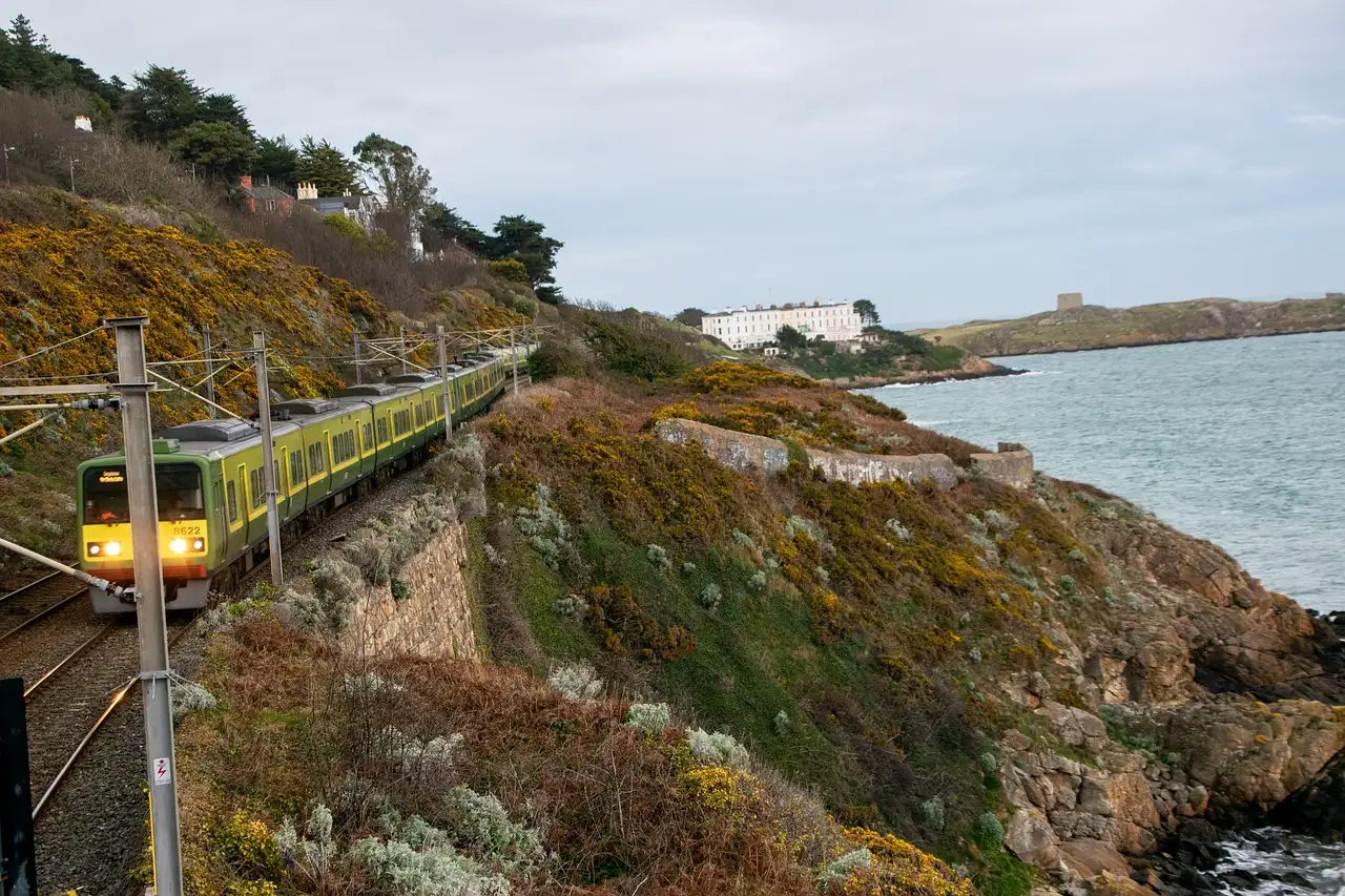 A green DART commuter train running along the rocky coast south of Dublin, with the sea on the right