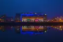 A Dublin riverside building lit blue at night and reflected in the water