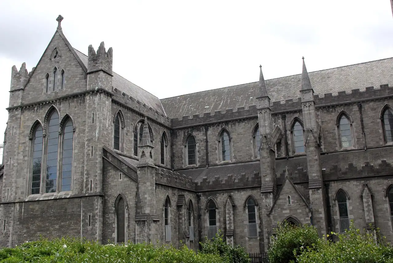 The long grey stone side of Christ Church Cathedral in Dublin, behind a green lawn