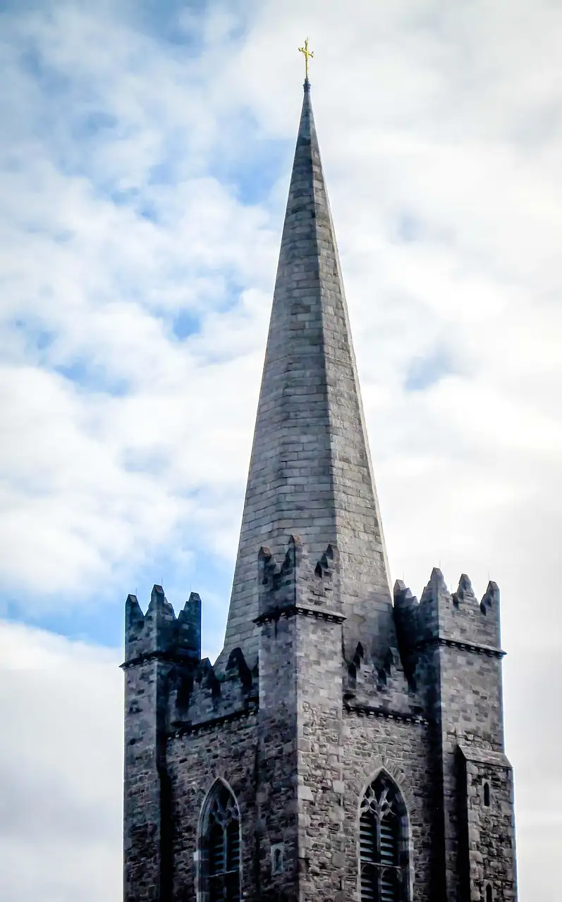 The stone tower and tall spire of St Patrick's Cathedral against a cloudy sky