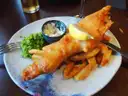 Fish and chips with mushy peas and a lemon wedge on a plate