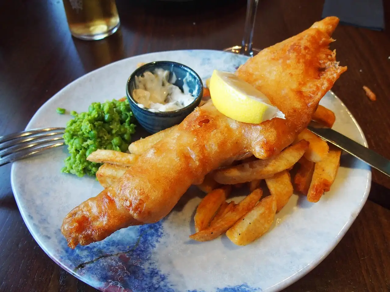 Fish and chips with mushy peas and a lemon wedge on a plate