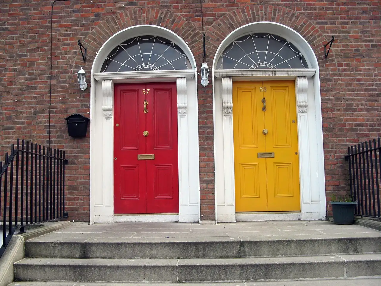 A red door and a yellow door side by side under fanlights in a Dublin red-brick terrace