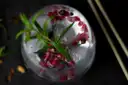 A gin glass with ice, rosemary and pomegranate seeds