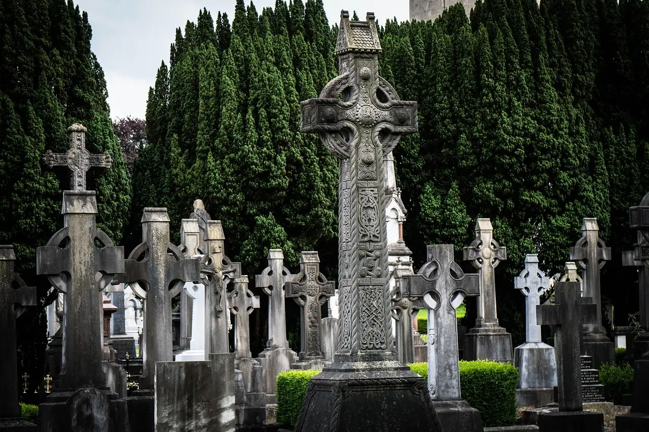 A tall carved Celtic cross among graves and dark yew trees at Glasnevin Cemetery