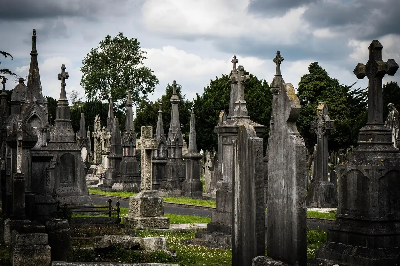 Rows of tall stone crosses and grave monuments at Glasnevin Cemetery under a cloudy sky