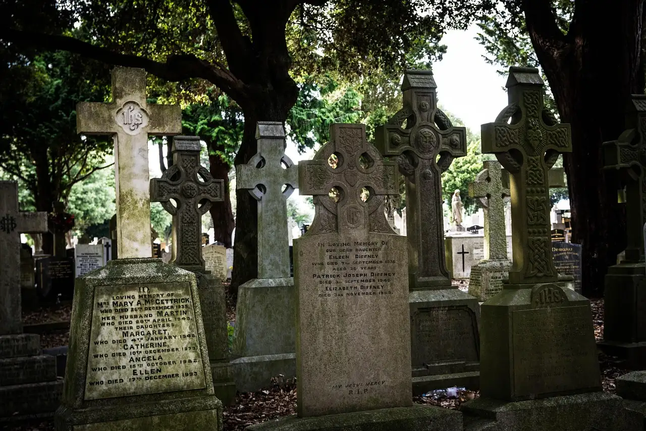 Old stone crosses and headstones in the shade of trees at Glasnevin Cemetery