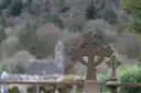A stone Celtic cross in front of the old monastic buildings at Glendalough