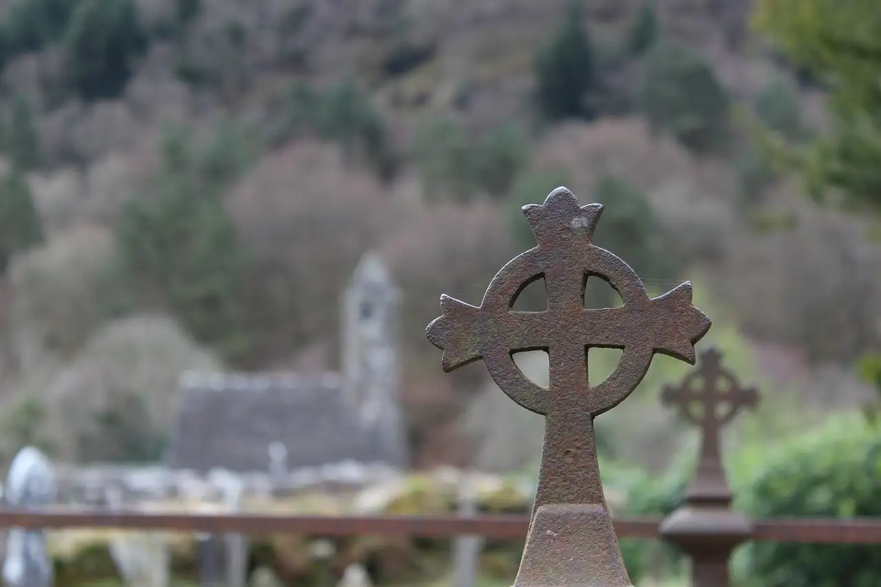 A stone Celtic cross in front of the old monastic buildings at Glendalough