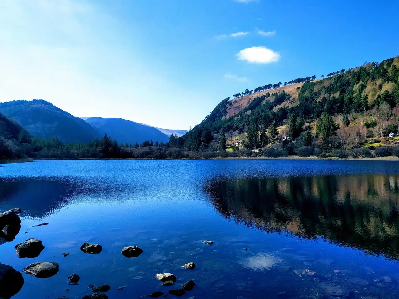A Glendalough lake reflecting wooded hills under a blue sky