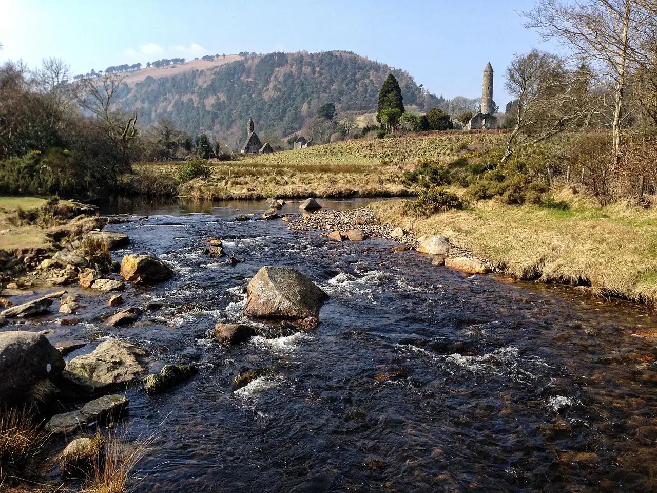 A rocky river in the Glendalough valley, with the round tower and green hills behind