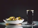 A pint of dark stout with a creamy head on a table, next to a bowl of crisps