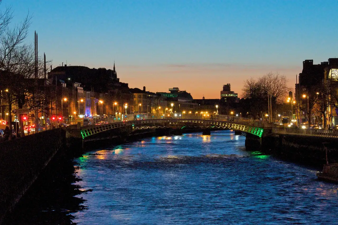 The Ha'penny Bridge lit up over the River Liffey at dusk, with the quays glowing behind