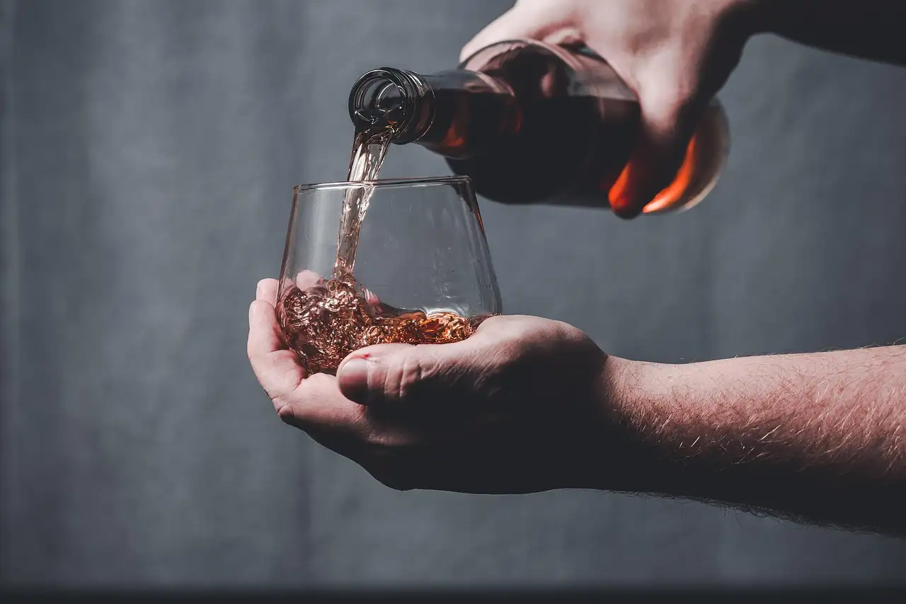 Whiskey being poured from a bottle into a glass held in a cupped hand