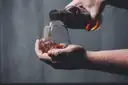 Whiskey being poured from a bottle into a glass held in a cupped hand