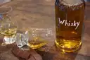 A bottle of whisky, two tasting glasses and squares of chocolate on a wooden table