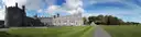 Kilkenny Castle beside its wide lawn and a path, under a blue sky