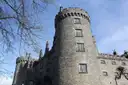 A round stone tower of Kilkenny Castle against a blue sky, with bare branches in front