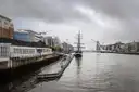 A tall ship moored on the River Liffey in Dublin's Docklands, with the harp-shaped bridge behind