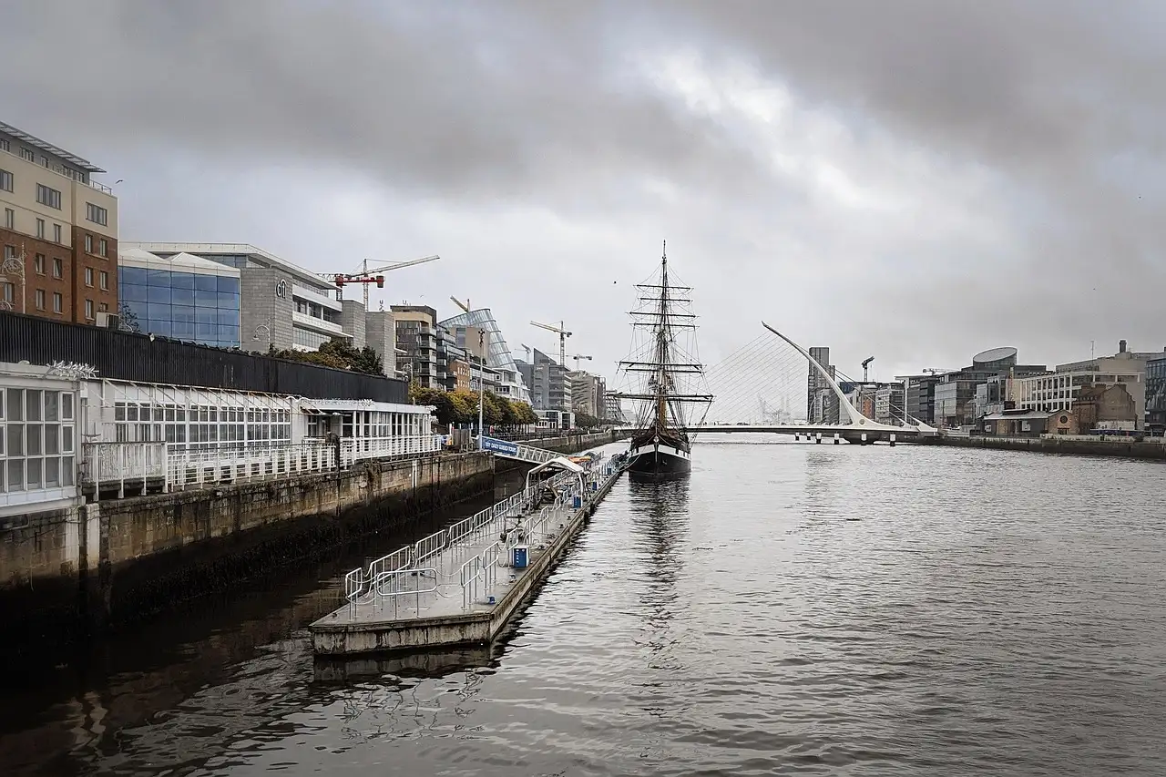A tall ship moored on the River Liffey in Dublin's Docklands, with the harp-shaped bridge behind