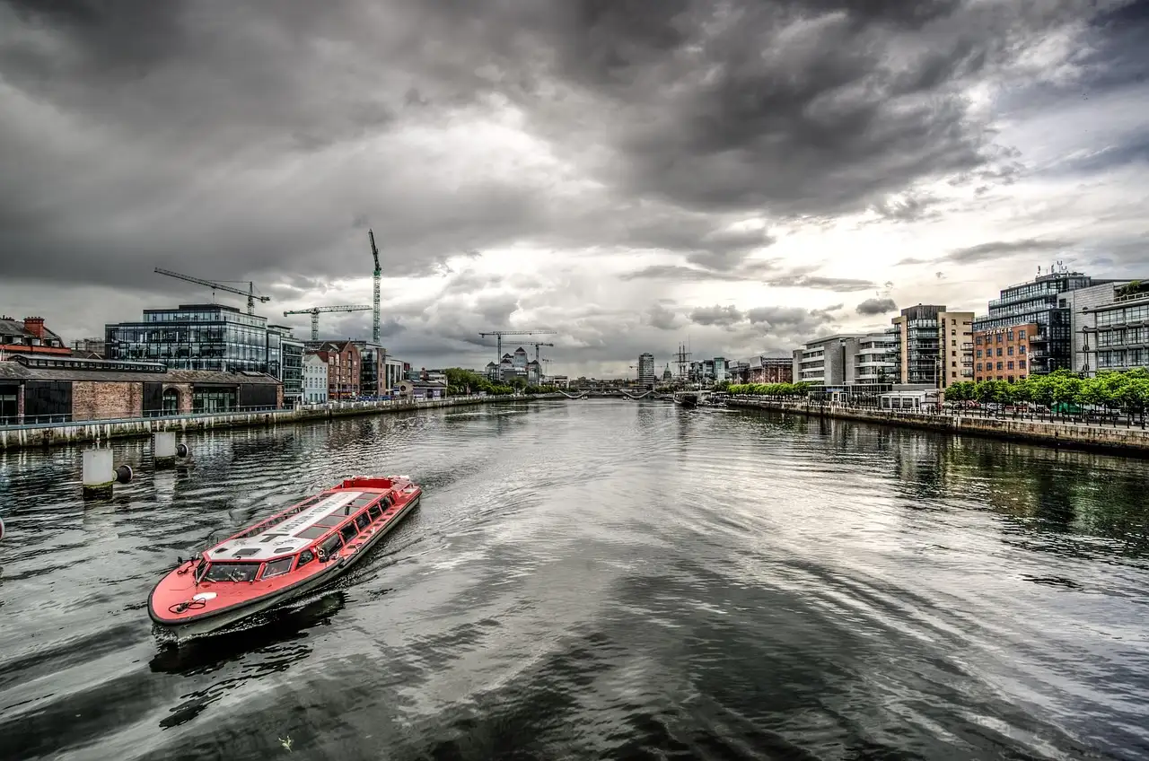 A red river boat on the River Liffey in the Dublin Docklands under grey clouds