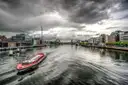 A red river boat on the River Liffey in the Dublin Docklands under grey clouds