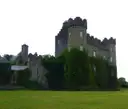 Malahide Castle, a grey stone castle with round towers, seen across the lawn