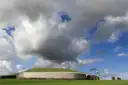 The grass-topped mound of Newgrange with its white stone front, under big clouds